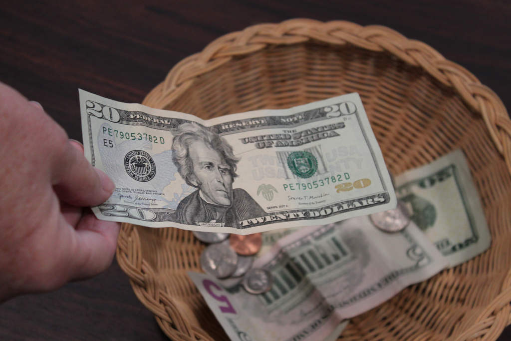 Hand putting money in a donation basket.